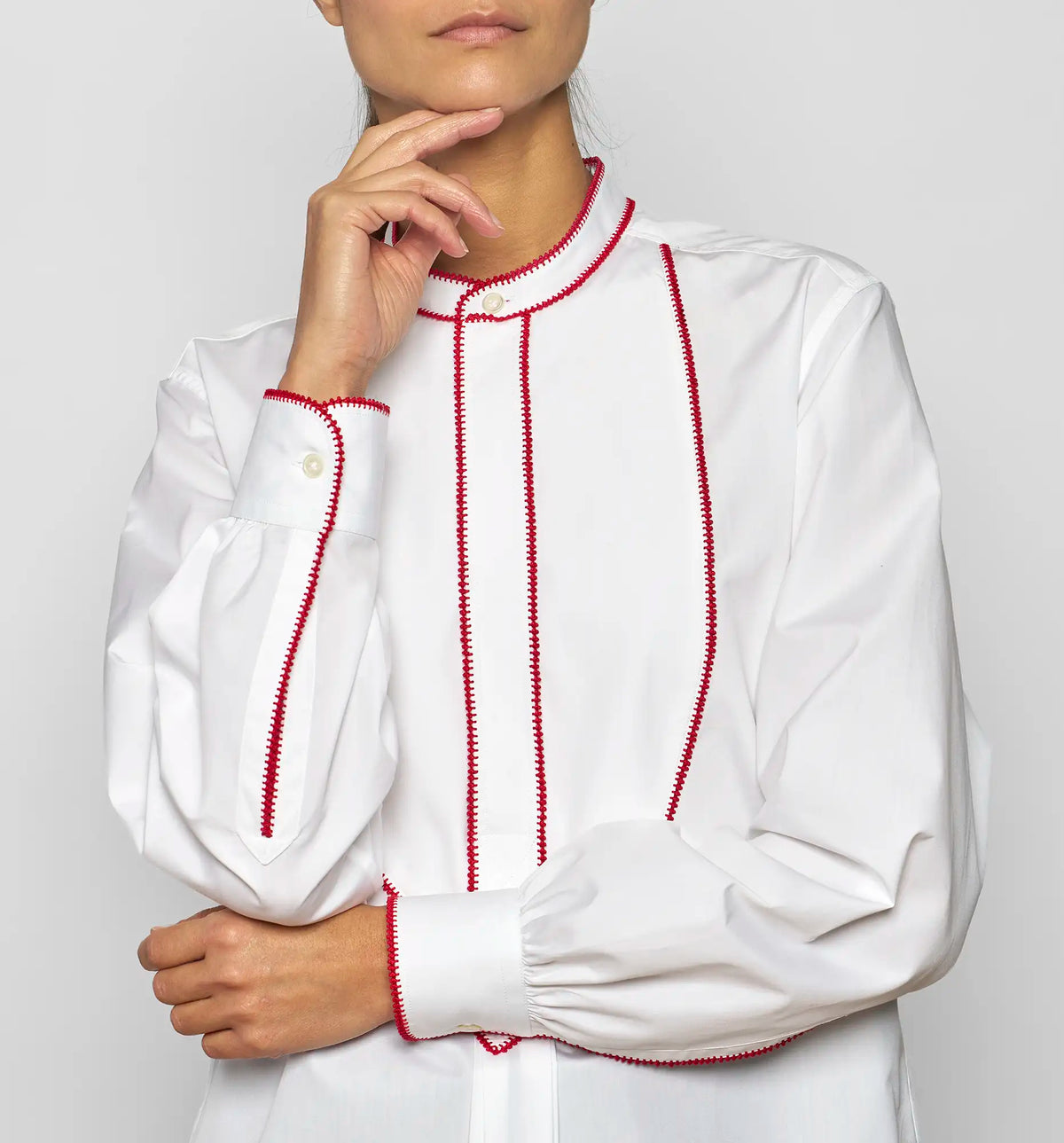 Detail of red embroidered stitch on the front bib of a white cotton poplin shirt by Sébline.