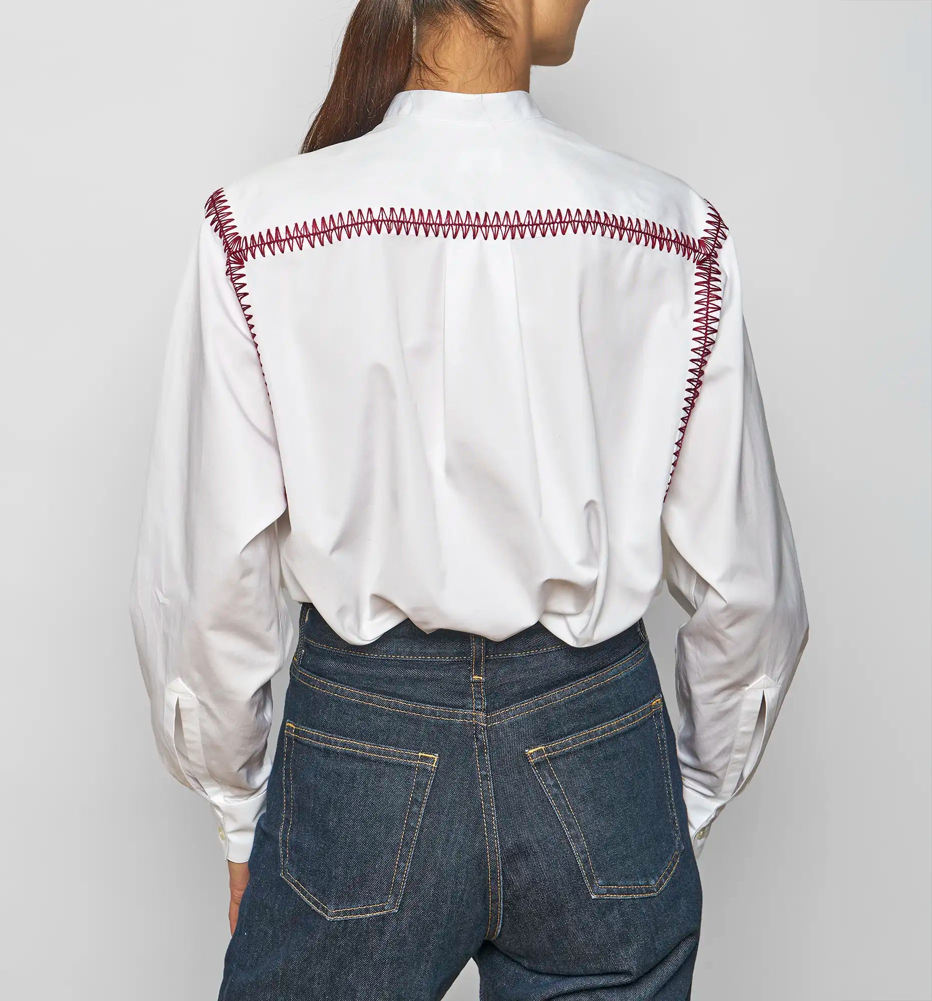 Model wearing a white Sébline pullover shirt with bordeaux embroidered bib, front view.