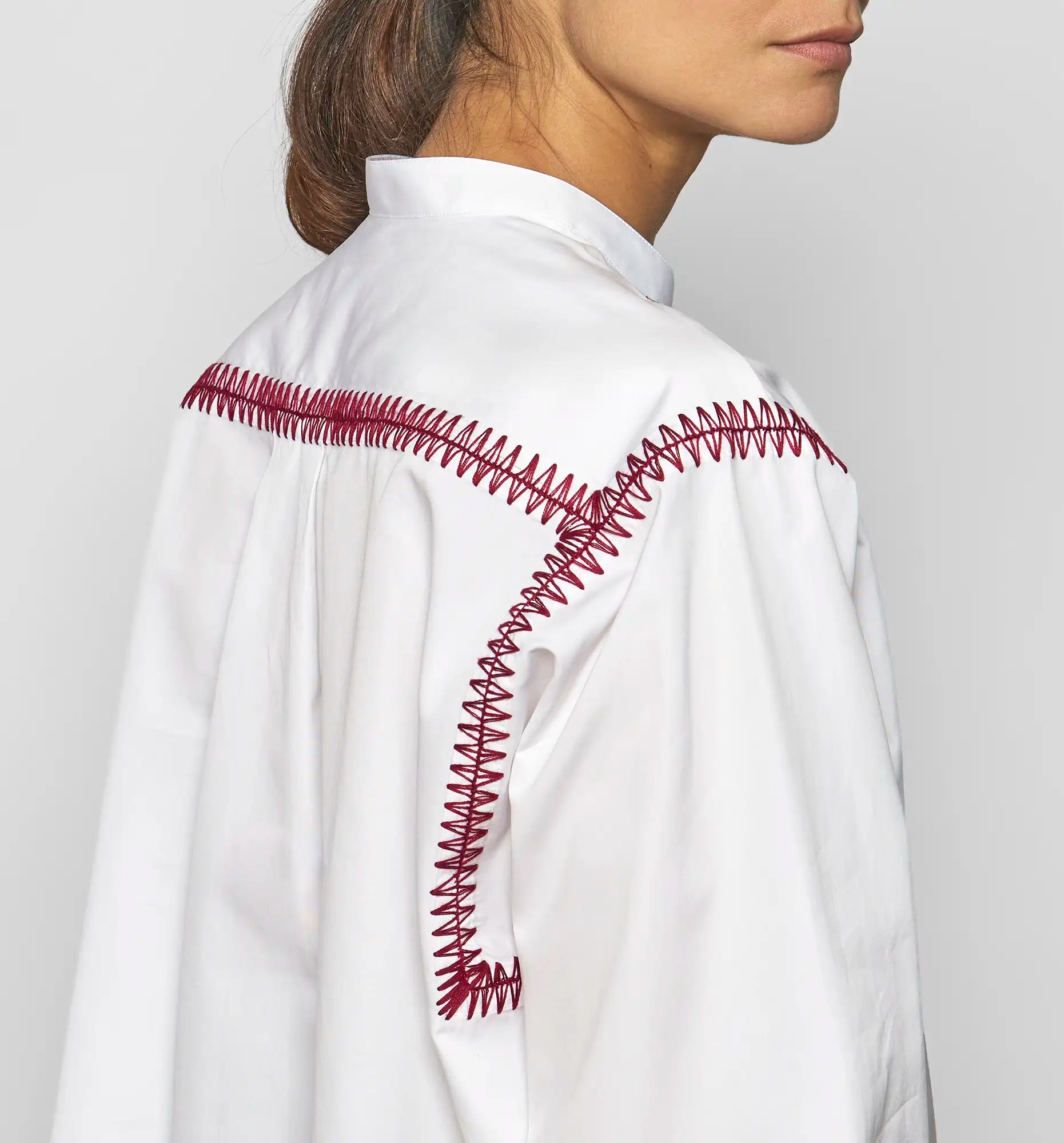 Close-up of bordeaux embroidery on the shoulder of a white Sébline pullover shirt.