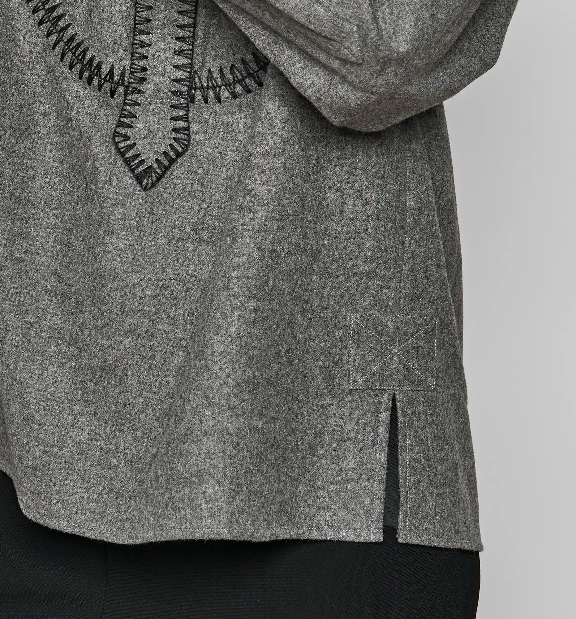 Close-up of the side hem and slit on a charcoal Sébline pullover shirt worn by a model.