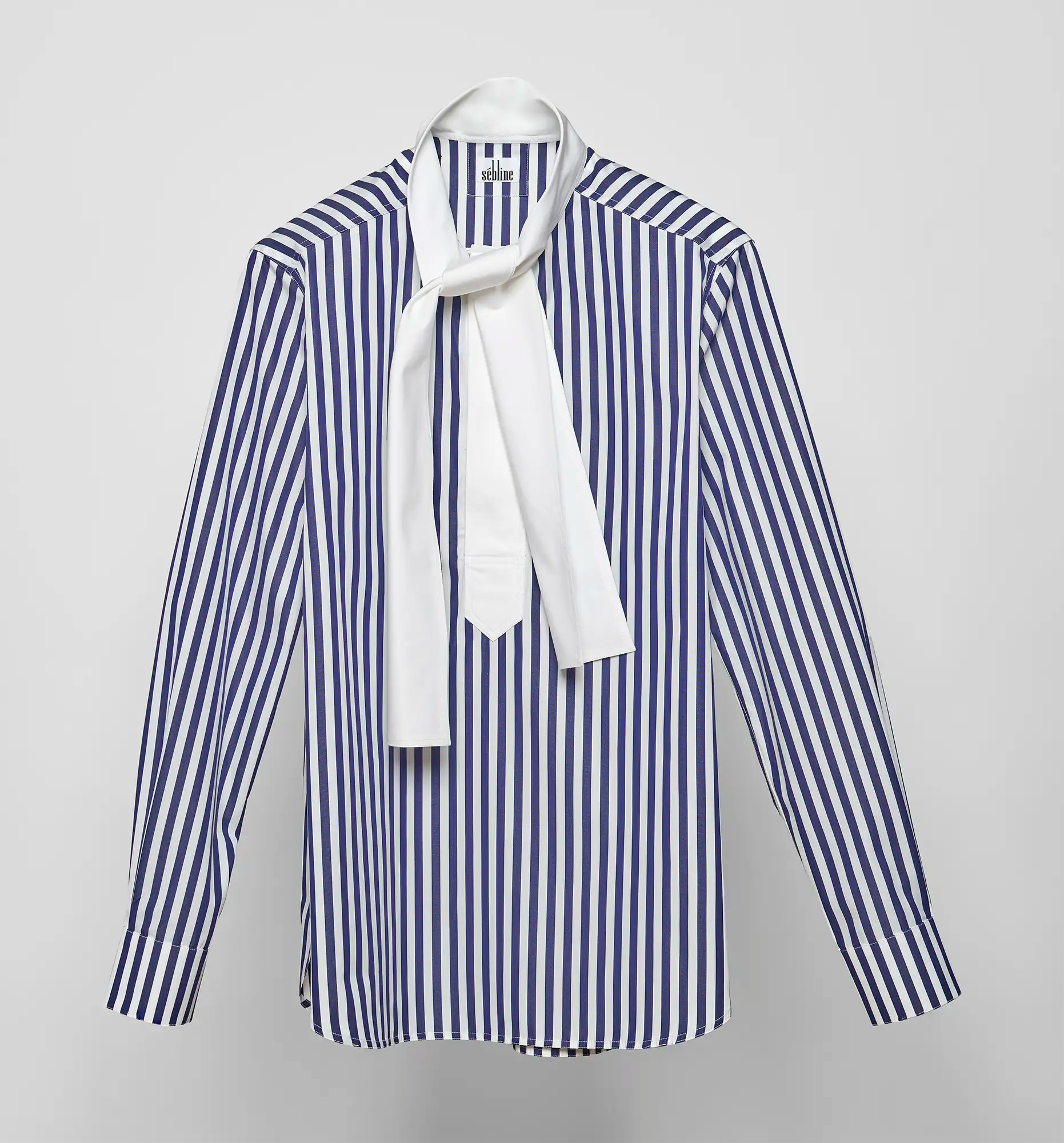 Front view of a navy and white striped Sébline shirt with a white necktie on a neutral background