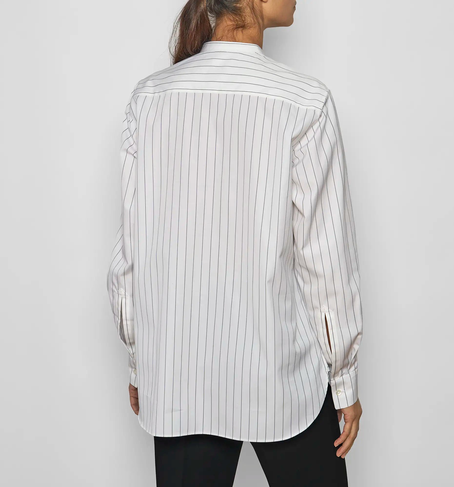 Model wearing a Sébline white long-sleeve pinstripe shirt with a striped bib, front view with the shirt worn untucked.