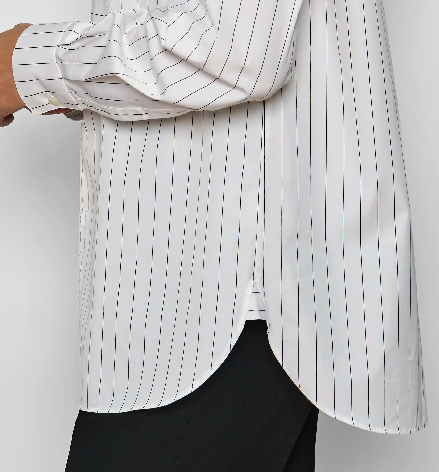 Close-up of the hem of a Sébline white pinstripe shirt on model, showing a curved hem.